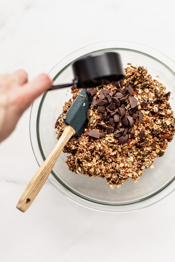 一只手把巧克力块倒进一碗超级食品格兰诺拉燕麦棒的原料中